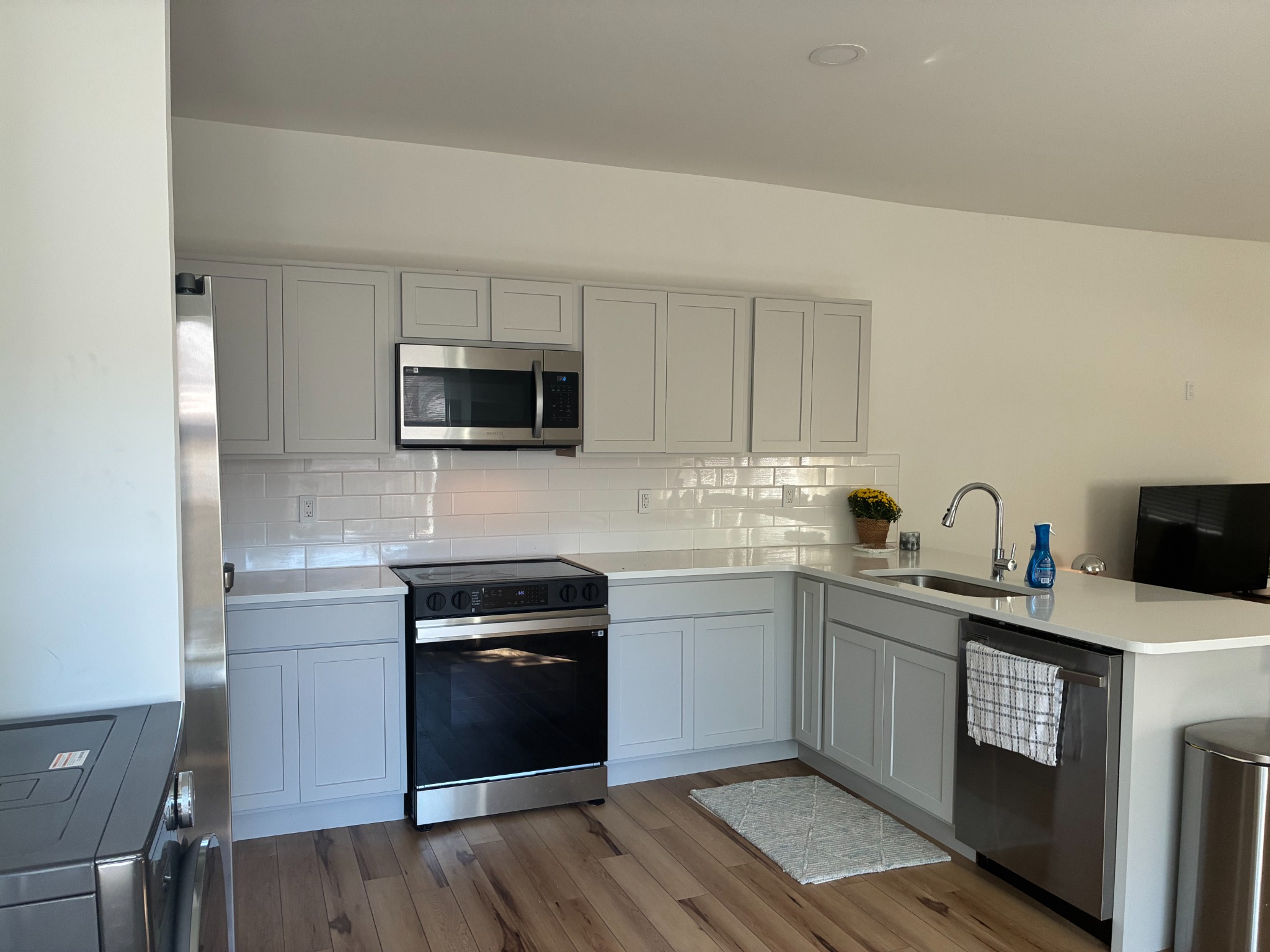 Wider view of the finished kitchen showing added cabinets, white tile backsplash and wood-look vinyl plank flooring