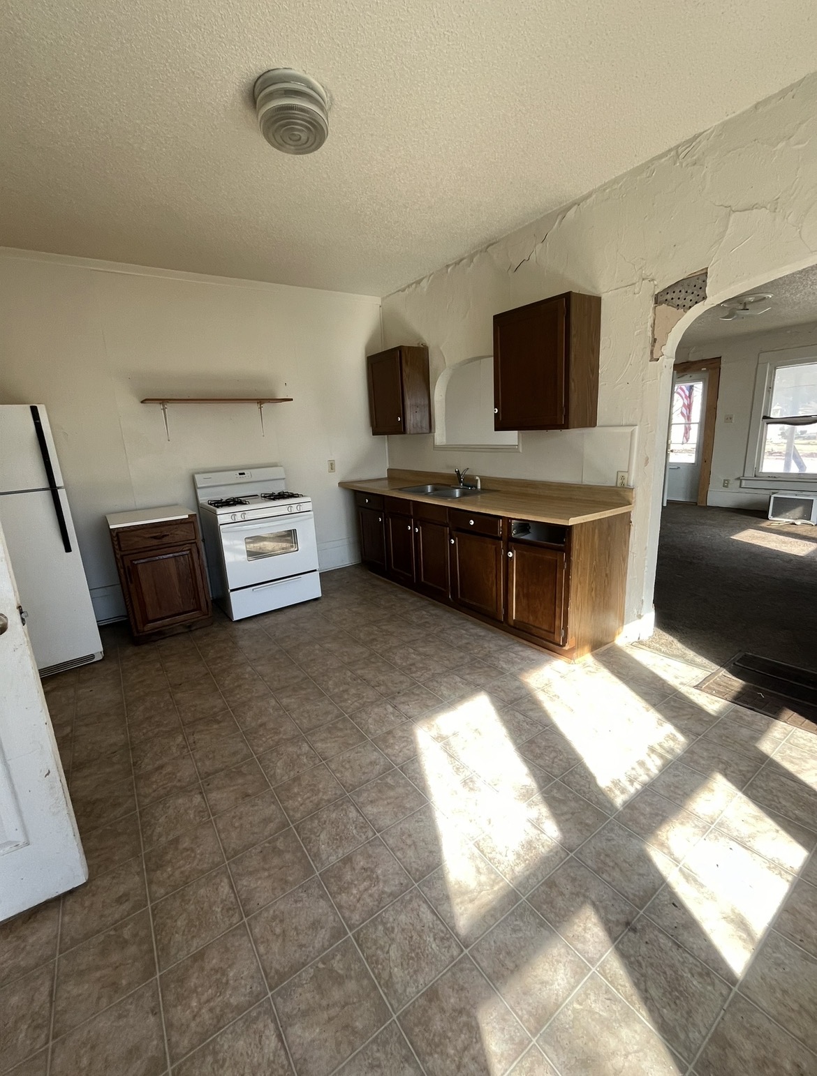 Wider view of the original rental kitchen showing limited cabinetry and the opening to the adjoining room
